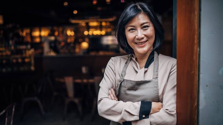 A restaurant owner smiling and wearing an apron with her arms folded.