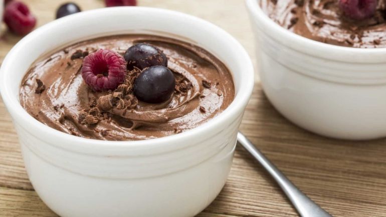 Chocolate mousse in a white ramekin with blueberries and raspberries on top.